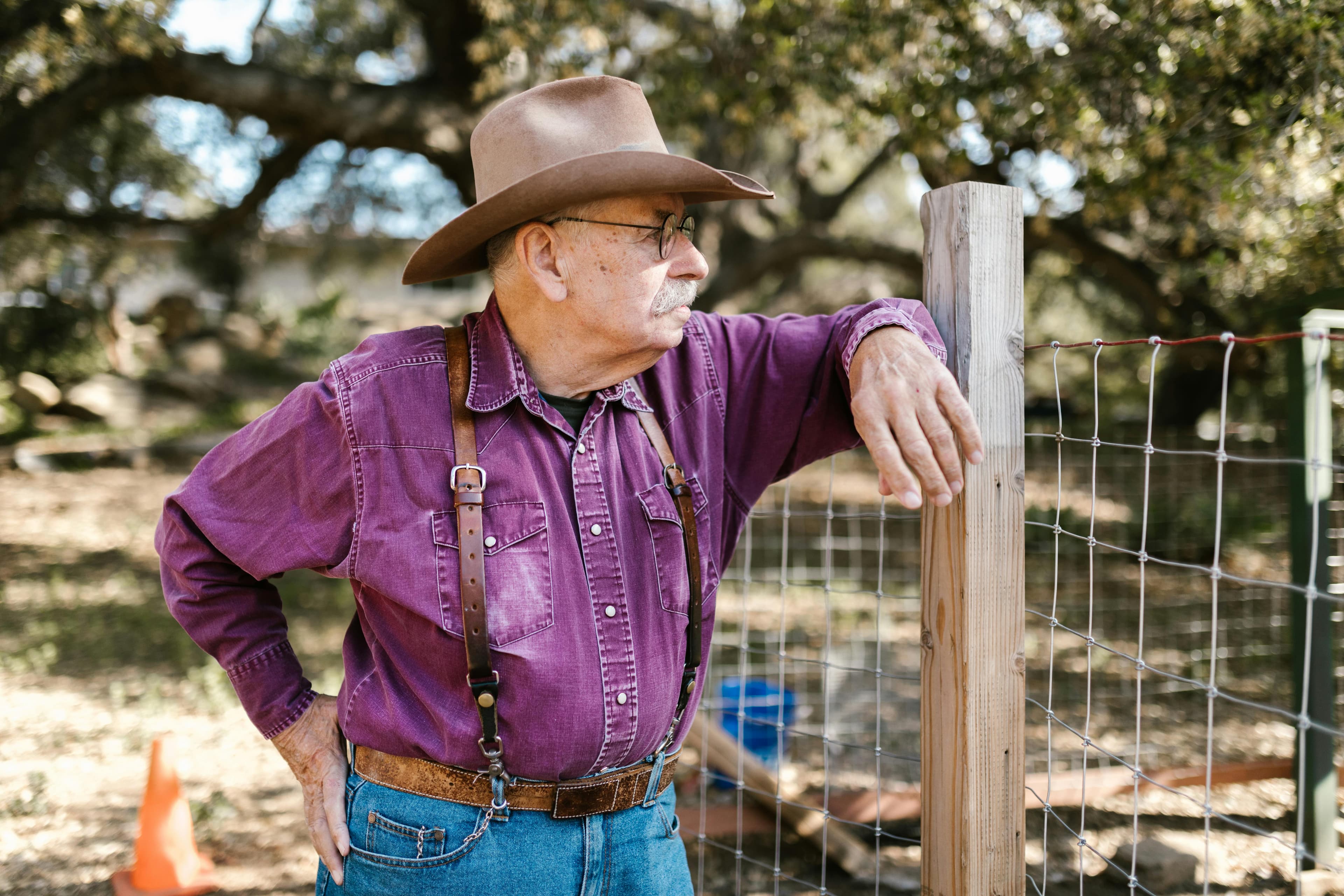 Texas rancher in cowboy hat tightening a wire fence at his property line